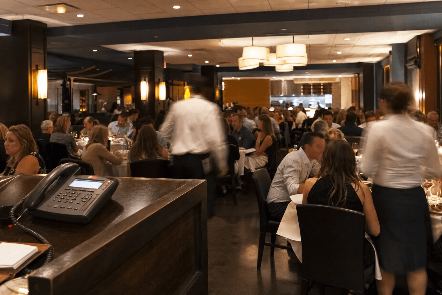 Packed restaurant dining room at dinner with a ringing phone at the host stand